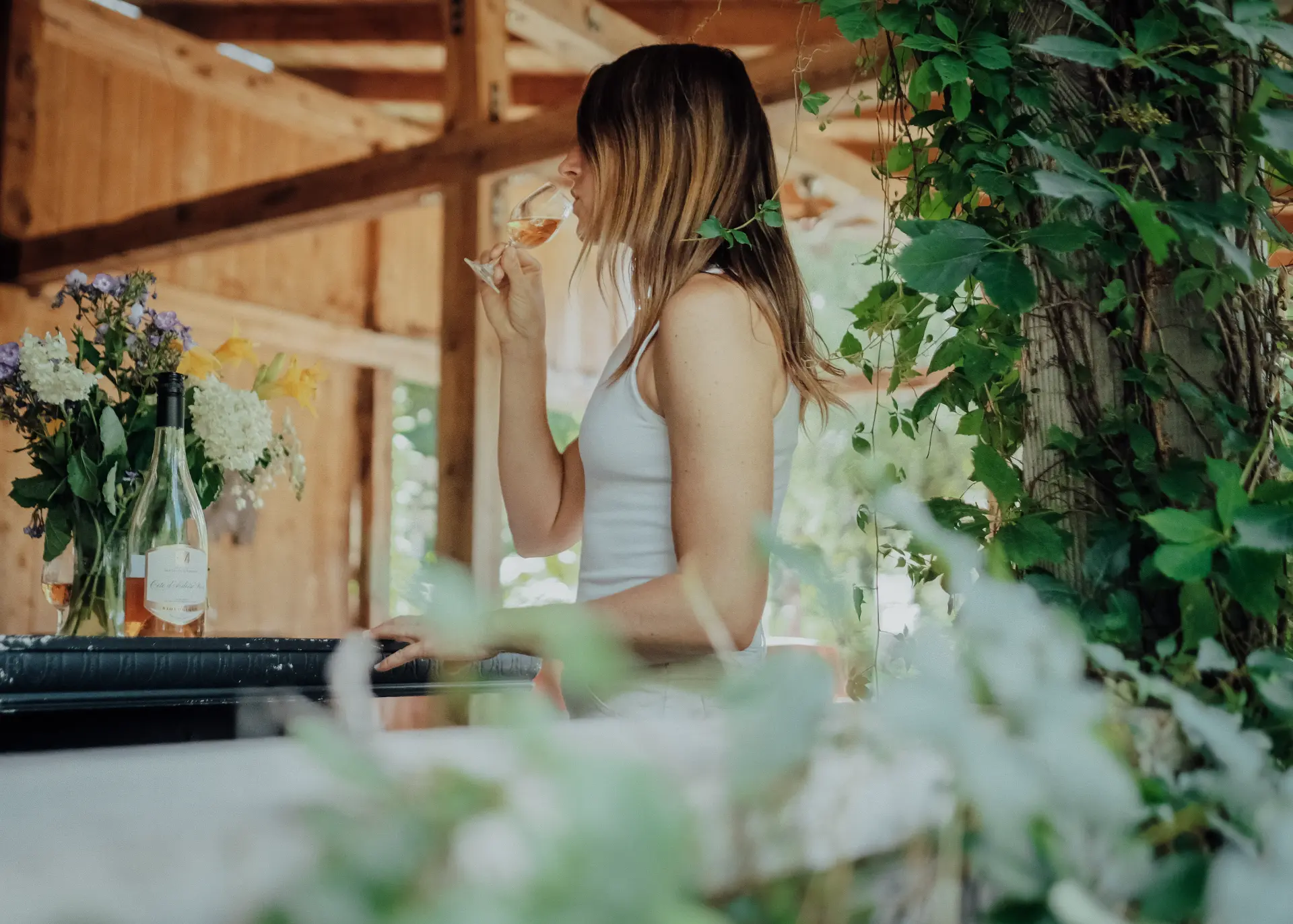 degustation vin rose route des vins brome missisquoi Femme dégustant un verre de vin rosé dans un vignoble des Cantons-de-l'Est, sur la Route des vins de Brome-Missisquoi, avec une bouteille et des fleurs.