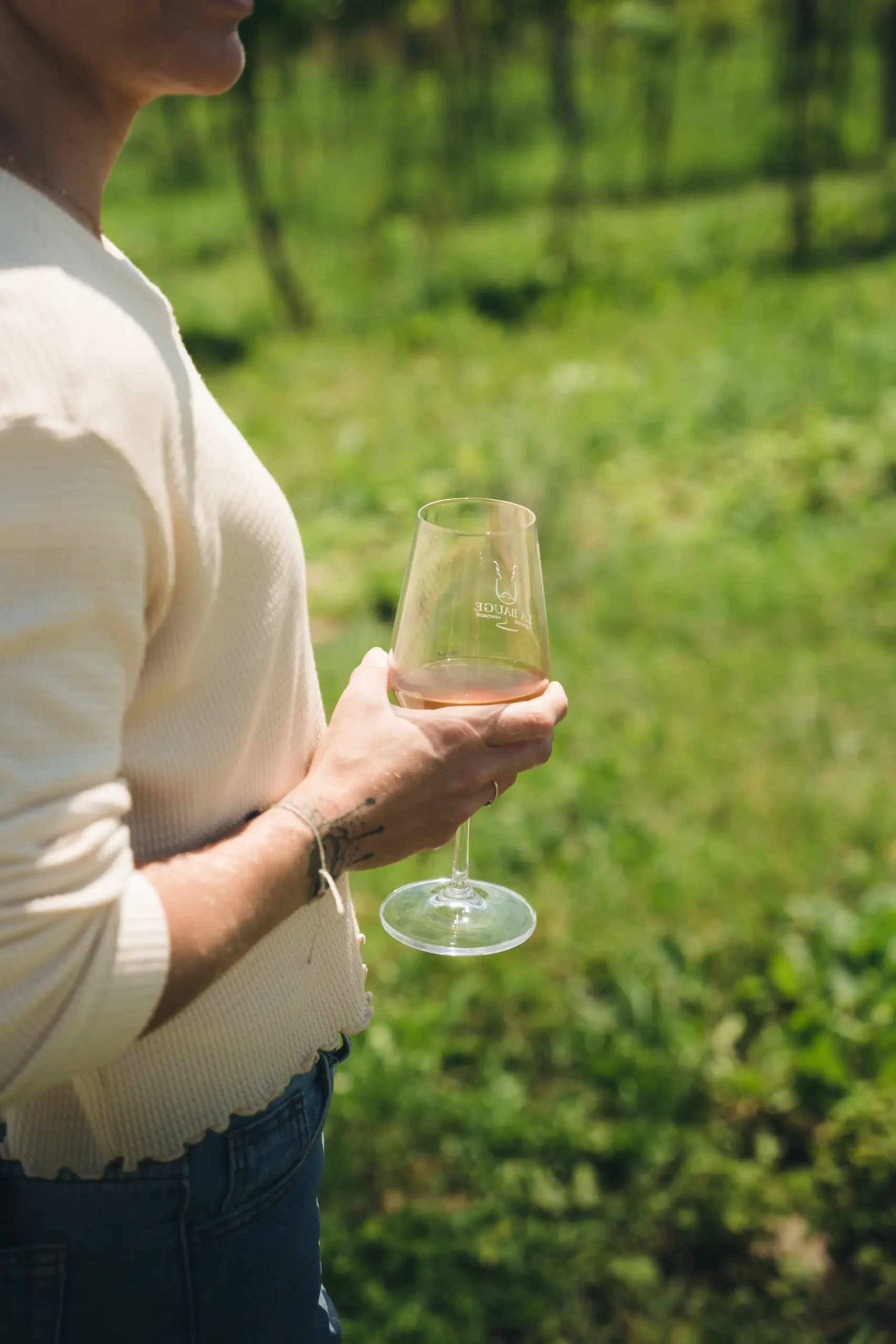 femme verre vin rose route des vins brome missisquoi scaled Main tenant un verre de vin rosé dans un vignoble ensoleillé. Dégustation sur la Route des vins de Brome-Missisquoi, Cantons-de-l'Est.