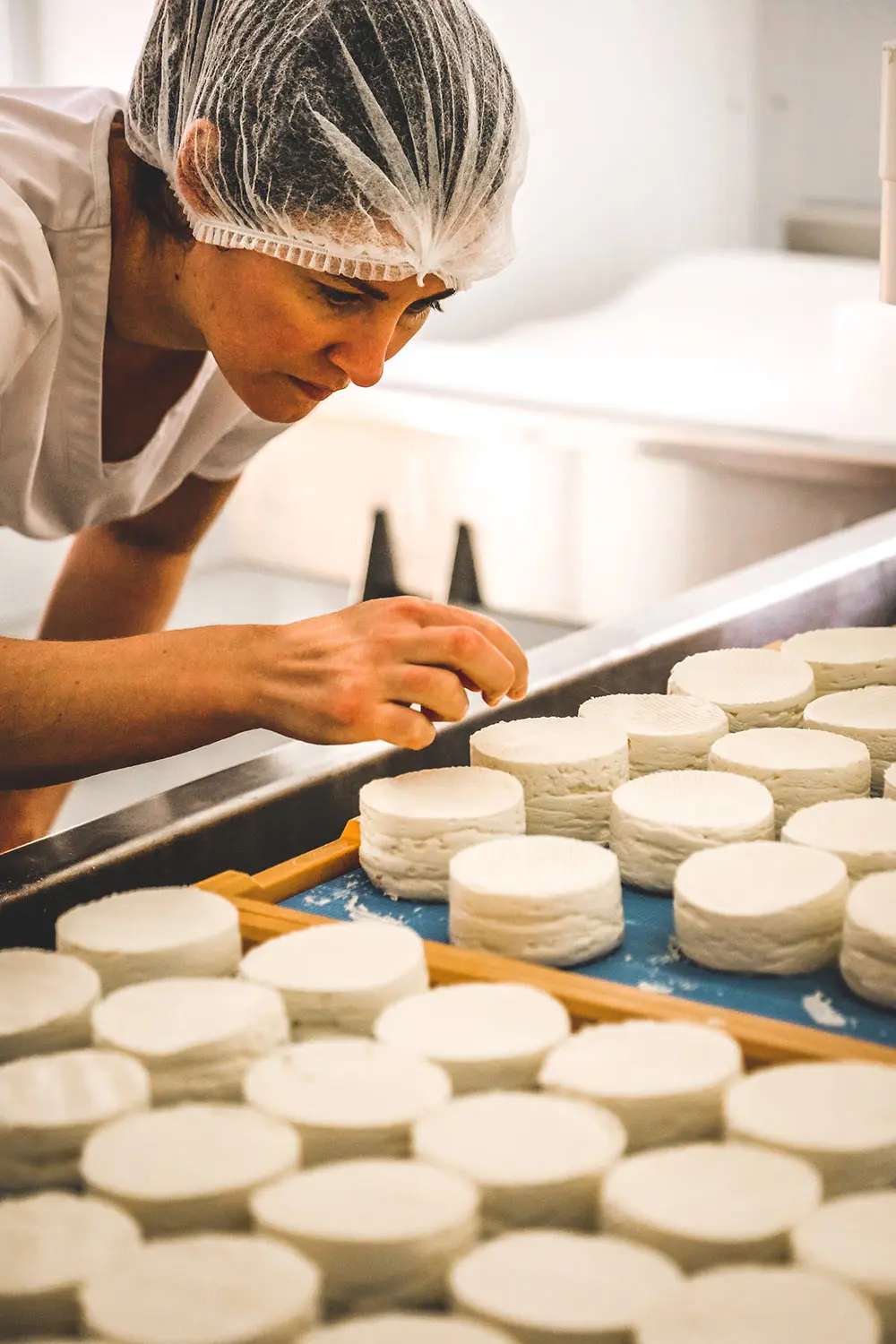 fromage artisanal brome missisquoi Fromagère en tenue de travail manipulant des fromages frais sur une ligne de production. Artisanat local des Cantons-de-l'Est, complémentaire à la Route des vins.